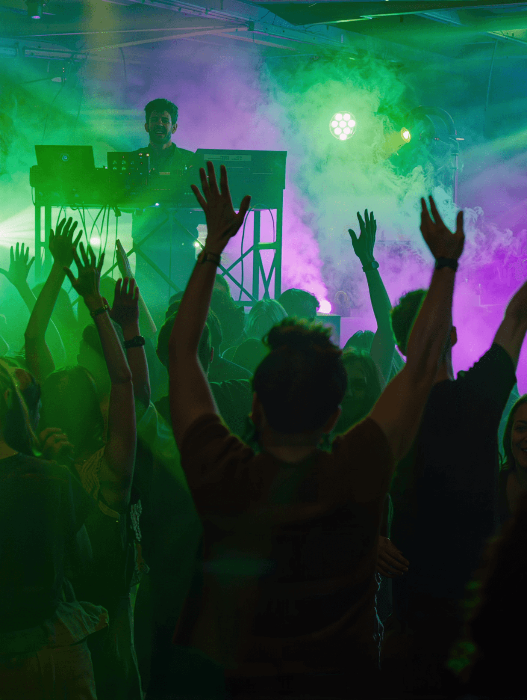 Crowd with hands up at a MINT DJ night under green and purple lights